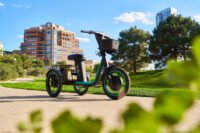 Veo's Rover electric trike, featuring three wheels, a cushioned seat, and baskets, in an urban setting.