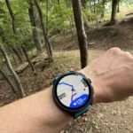 A runner checking their GPS smartwatch with a map display on a scenic trail.
