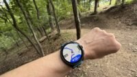 A runner checking their GPS smartwatch with a map display on a scenic trail.
