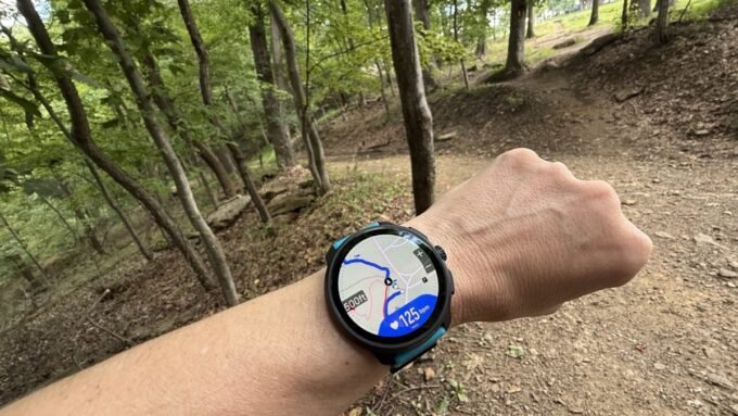 A runner checking their GPS smartwatch with a map display on a scenic trail.