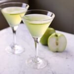 Vibrant green Appletini cocktail garnished with a fresh apple slice in a chilled martini glass.