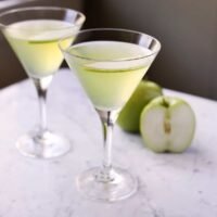 Vibrant green Appletini cocktail garnished with a fresh apple slice in a chilled martini glass.