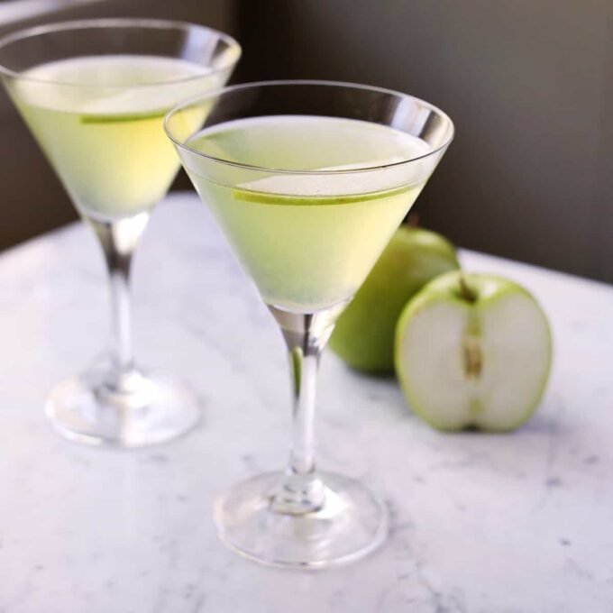 Vibrant green Appletini cocktail garnished with a fresh apple slice in a chilled martini glass.