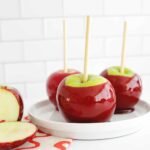 Vibrant red candy apples on sticks, glistening and ready to eat, set against an autumnal backdrop.