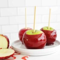 Vibrant red candy apples on sticks, glistening and ready to eat, set against an autumnal backdrop.