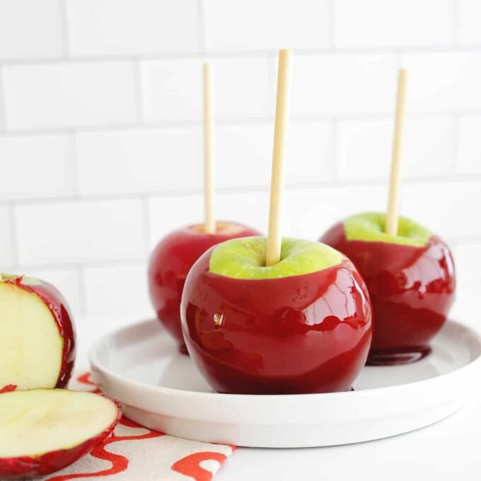 Vibrant red candy apples on sticks, glistening and ready to eat, set against an autumnal backdrop.