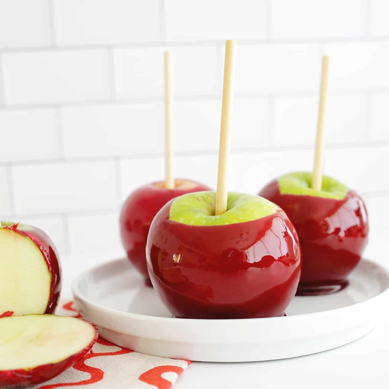 Vibrant red candy apples on sticks, glistening and ready to eat, set against an autumnal backdrop.