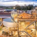 Vue aérienne d'une mine d'or ivoirienne en exploitation, avec des équipements lourds et des structures industrielles, sous un ciel clair.