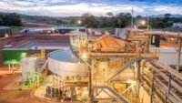 Vue aérienne d'une mine d'or ivoirienne en exploitation, avec des équipements lourds et des structures industrielles, sous un ciel clair.