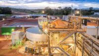 Vue aérienne d'une mine d'or ivoirienne en exploitation, avec des équipements lourds et des structures industrielles, sous un ciel clair.