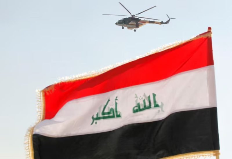 صورة جوية للعلم العراقي يرفرف فوق قاعدة عسكرية في بغداد، مع مروحية تحلق في السماء.