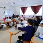صورة لساعة حائط تشير إلى الثامنة صباحًا في فصل دراسي، أو مدخل مؤسسة تعليمية مغربية.
