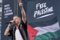 صورة لمغني الراب ماكلمور يؤدي على المسرح، أو لافتة لدعم فلسطين في حفل موسيقي.