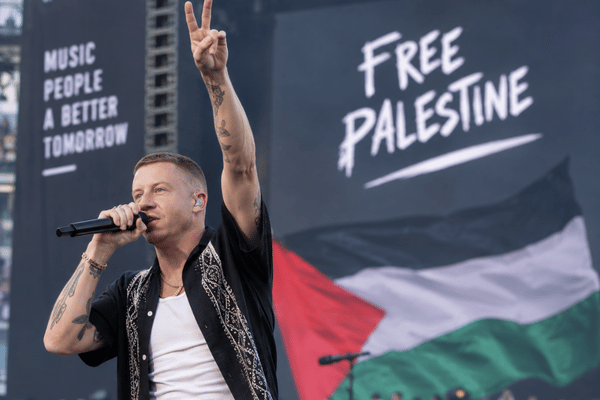 صورة لمغني الراب ماكلمور يؤدي على المسرح، أو لافتة لدعم فلسطين في حفل موسيقي.