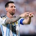 ليونيل ميسي يرتدي قميص منتخب الأرجنتين ويحيي الجماهير في ملعب كرة قدم.