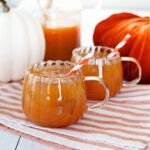 A glass of homemade Harry Potter Pumpkin Juice, garnished with a pumpkin-shaped glass and an orange striped straw.