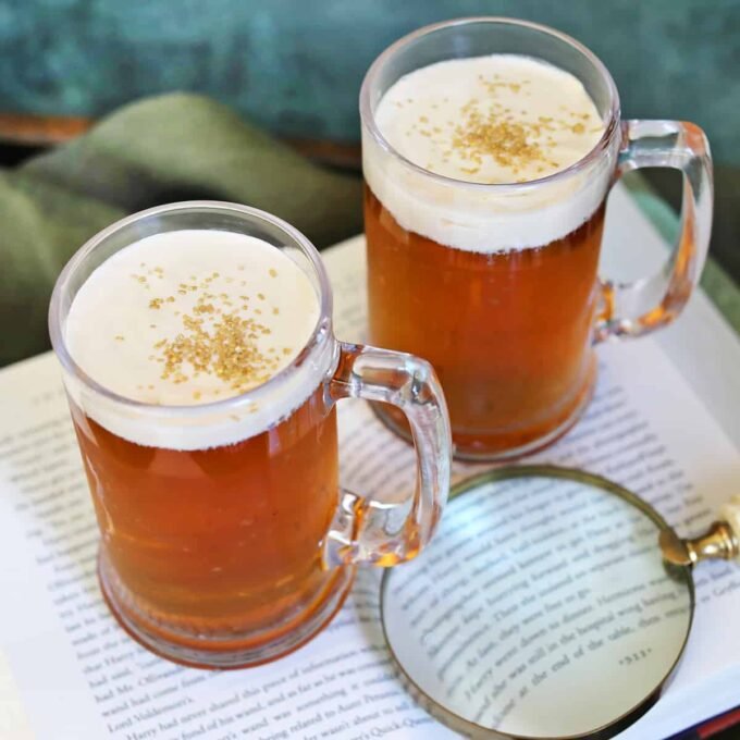 A frosty mug of homemade Butterbeer with a thick caramel foam topping and gold sprinkles, reminiscent of the drink from Harry Potter's Wizarding World.