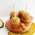 A perfectly coated caramel apple adorned with various toppings like nuts, sprinkles, and chocolate, ready to be enjoyed.