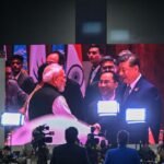 Indian Prime Minister Narendra Modi and Chinese President Xi Jinping meeting during the 18th BRICS Summit in New Delhi, displayed on a large digital screen.