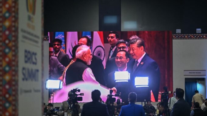 Indian Prime Minister Narendra Modi and Chinese President Xi Jinping meeting during the 18th BRICS Summit in New Delhi, displayed on a large digital screen.