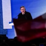 Jean-Luc Mélenchon s'adressant à la foule lors de la Fête de l'Humanité, avec des drapeaux de La France Insoumise et de la NUPES en arrière-plan, symbolisant son appel à l'unité de la gauche pour 2027.