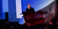 Jean-Luc Mélenchon s'adressant à la foule lors de la Fête de l'Humanité, avec des drapeaux de La France Insoumise et de la NUPES en arrière-plan, symbolisant son appel à l'unité de la gauche pour 2027.