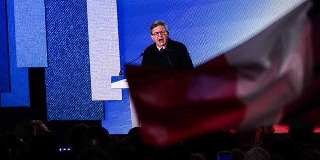 Jean-Luc Mélenchon s'adressant à la foule lors de la Fête de l'Humanité, avec des drapeaux de La France Insoumise et de la NUPES en arrière-plan, symbolisant son appel à l'unité de la gauche pour 2027.