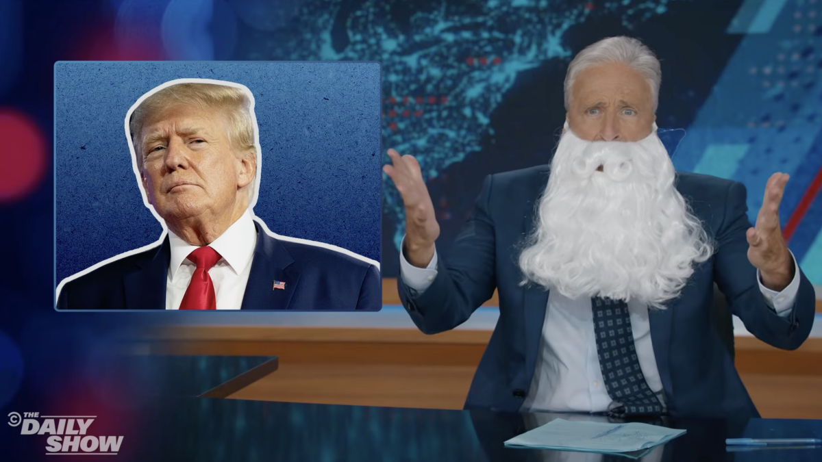 Jon Stewart with a long white beard, looking exasperated at The Daily Show desk