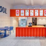 Interior view of The Kimchi restaurant in Prague, showcasing the blue tables, red-grouted white tiles, and the fluid wave design element.