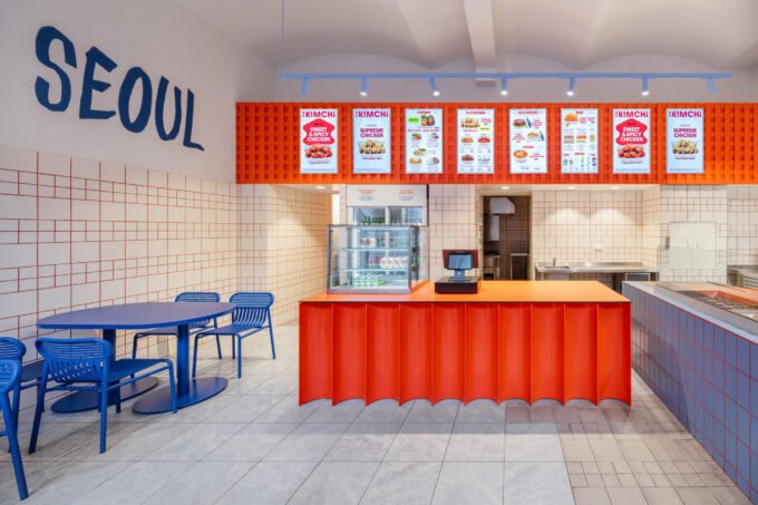 Interior view of The Kimchi restaurant in Prague, showcasing the blue tables, red-grouted white tiles, and the fluid wave design element.