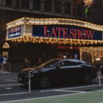 A collage or graphic representing various late-night talk show hosts and their iconic sets, symbolizing the enduring spirit of late-night television.