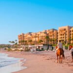 Mazagan propose jusqu’à 20 % de réduction sur l’hébergement et les soins Spa 6 Vue panoramique du Mazagan Beach & Golf Resort au coucher du soleil, avec la plage et le parcours de golf en arrière-plan, illustrant une évasion luxueuse et relaxante.
