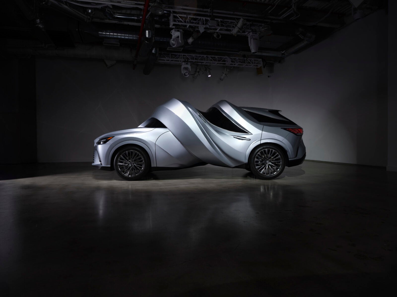 Surreal automotive sculptures by MSCHF, a Lexus RZ 450e twisted into a circle and an RX 450h+ spiraled, displayed at MOTOMORPHOSIS exhibition.