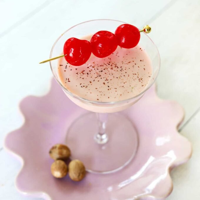 A vibrant pink Pink Squirrel cocktail in a coupe glass, garnished with a maraschino cherry and a sprinkle of nutmeg.