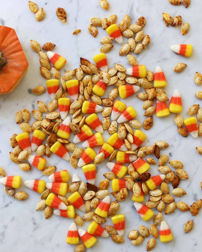 Autumn's Golden Crunch: Crafting the Perfect Roasted Pumpkin Seeds 7 A close-up of golden-brown roasted pumpkin seeds on a baking sheet, some mixed with colorful candy corn.