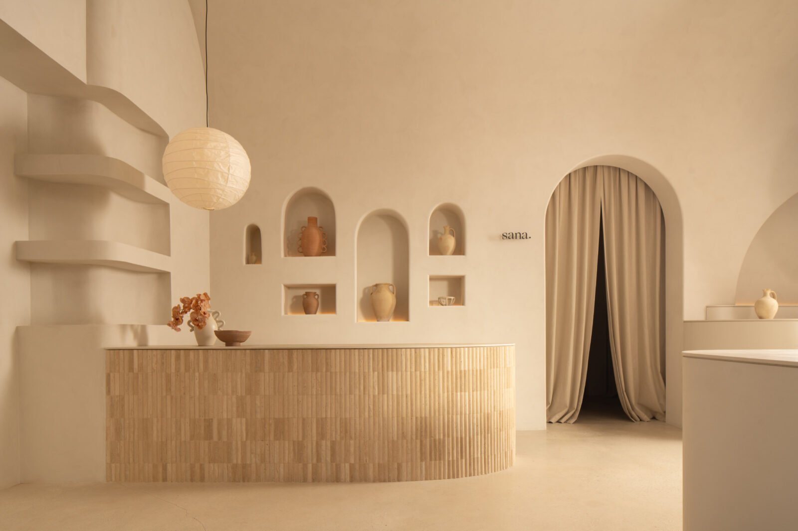 Interior view of Sana Skin Studio in Wynwood, showcasing its high ceilings, arched doorways, and a circular illuminated feature with a soothing beige palette.