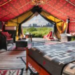 The Urban Cowboy Tent interior on Governors Island, featuring red Pendleton textiles, vintage furnishings, and a view of the Statue of Liberty.