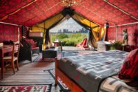 The Urban Cowboy Tent interior on Governors Island, featuring red Pendleton textiles, vintage furnishings, and a view of the Statue of Liberty.