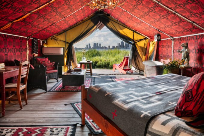 The Urban Cowboy Tent interior on Governors Island, featuring red Pendleton textiles, vintage furnishings, and a view of the Statue of Liberty.