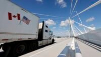 A truck crosses the Gordie Howe International Bridge, symbolizing the flow of trade between Windsor, Ontario, and Detroit, Michigan, amidst escalating US-Canada trade tensions.