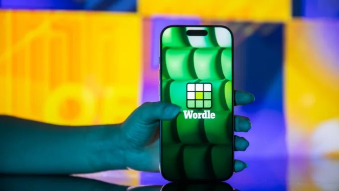 A Wordle game grid displaying green, yellow, and grey letter tiles, with a magnifying glass hovering over it.