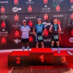 Vue aérienne de triathlètes nageant dans la baie d'Agadir lors de l'IRONMAN 70.3, avec la ville et les montagnes en arrière-plan, symbolisant le défi sportif et le cadre marocain.