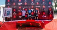 Vue aérienne de triathlètes nageant dans la baie d'Agadir lors de l'IRONMAN 70.3, avec la ville et les montagnes en arrière-plan, symbolisant le défi sportif et le cadre marocain.
