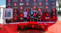 Vue aérienne de triathlètes nageant dans la baie d'Agadir lors de l'IRONMAN 70.3, avec la ville et les montagnes en arrière-plan, symbolisant le défi sportif et le cadre marocain.