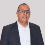 Amine Amanatoullah, Secrétaire général de la FIFEL, s'exprimant avec gravité sur les défis climatiques et hydriques qui menacent l'agriculture marocaine, notamment les cultures maraîchères du Souss-Massa, avec des serres en arrière-plan sous un ciel potentiellement nuageux ou ensoleillé.