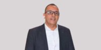 Amine Amanatoullah, Secrétaire général de la FIFEL, s'exprimant avec gravité sur les défis climatiques et hydriques qui menacent l'agriculture marocaine, notamment les cultures maraîchères du Souss-Massa, avec des serres en arrière-plan sous un ciel potentiellement nuageux ou ensoleillé.