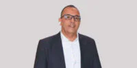 Amine Amanatoullah, Secrétaire général de la FIFEL, s'exprimant avec gravité sur les défis climatiques et hydriques qui menacent l'agriculture marocaine, notamment les cultures maraîchères du Souss-Massa, avec des serres en arrière-plan sous un ciel potentiellement nuageux ou ensoleillé.