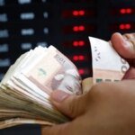 Le Maroc, champion du cash : 540 milliards de dirhams en circulation, le défi du numérique 6 Une pile de billets de dirhams marocains, avec un smartphone affichant une application de paiement mobile en arrière-plan, illustrant le paradoxe entre l'essor du cash et la digitalisation des paiements.