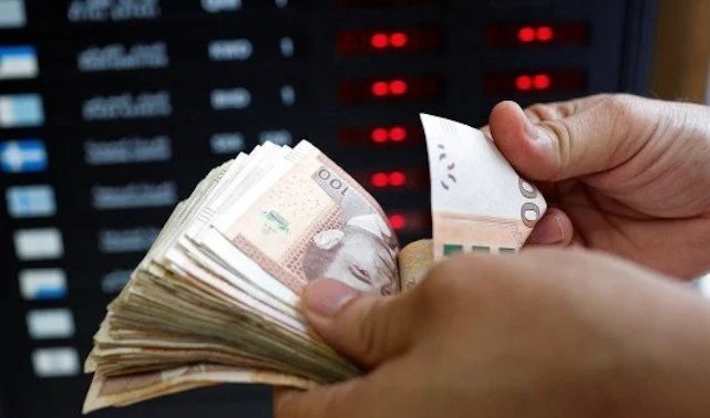 Le Maroc, champion du cash : 540 milliards de dirhams en circulation, le défi du numérique 7 Une pile de billets de dirhams marocains, avec un smartphone affichant une application de paiement mobile en arrière-plan, illustrant le paradoxe entre l'essor du cash et la digitalisation des paiements.