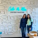 Antima Jain and Pooja Choudhary, co-owners of Color Me Mine Edina, smiling in their vibrant pottery studio.